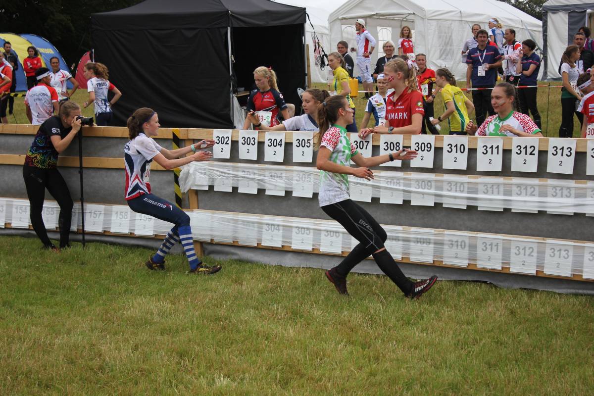 Megan Keith races in after completing Leg 1 - now to Fiona Bunn.    Photo credit:  IOF / JWOC 2019